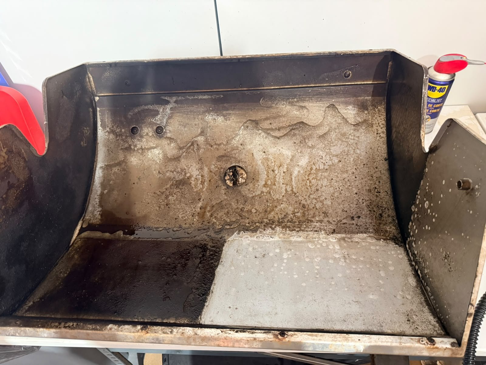 Grillkar i vårt verksted med fastbrent fett og svarte avleiringer på venstre halvdel og rengjort høyre halvdel, med en synlig skillelinje i midten.